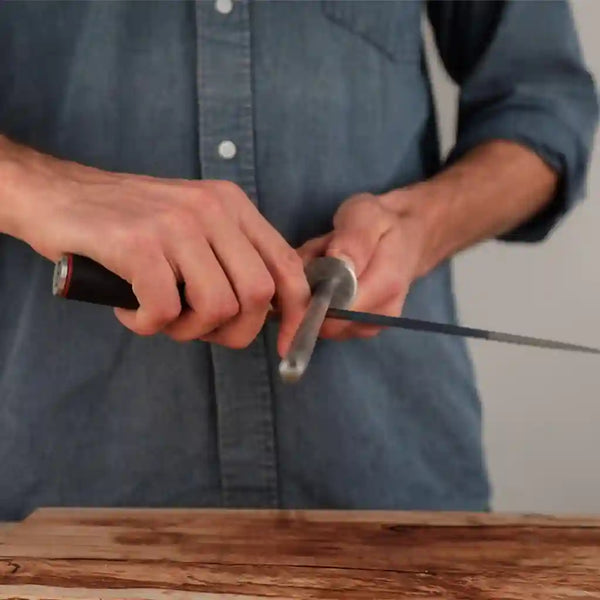 The model is stroking the knife with the honing steel towards the tip.