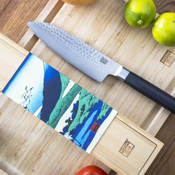 KOTAI's Santoku knife blade 18 cm kept on bamboo cutting board next to its bamboo box.