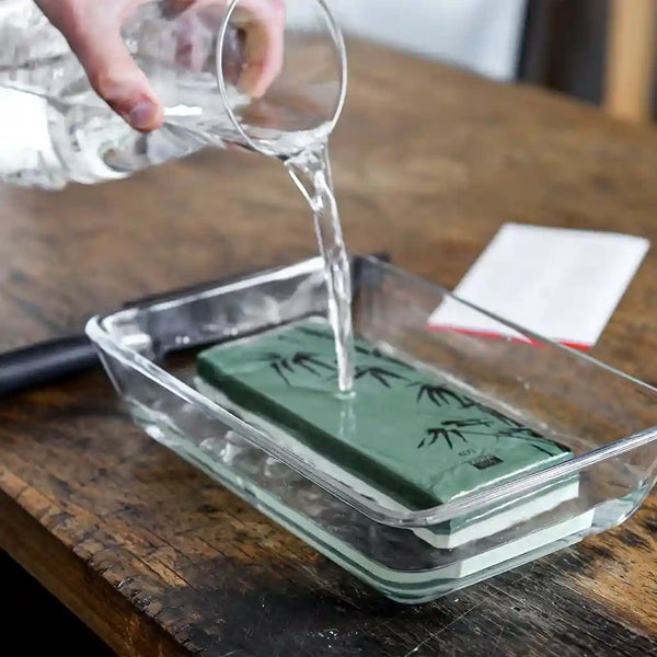 The model is pouring water on the KOTAI whetstone grit 400/1000 to soak it.