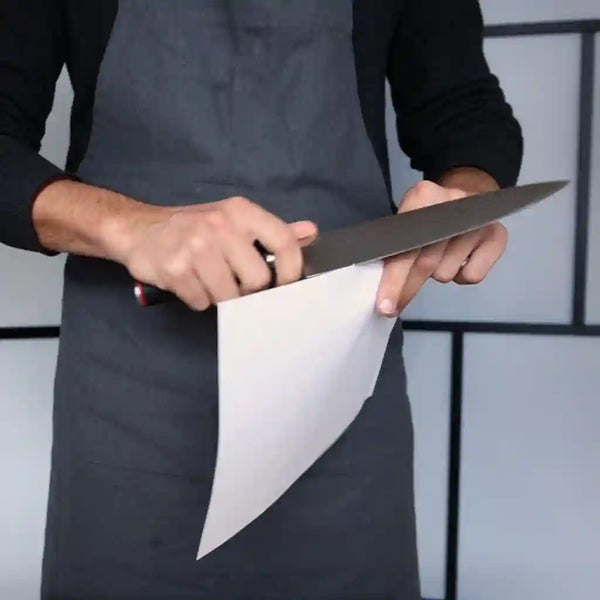 The model is testing the sharpness of the knife by cutting a piece of paper with it.