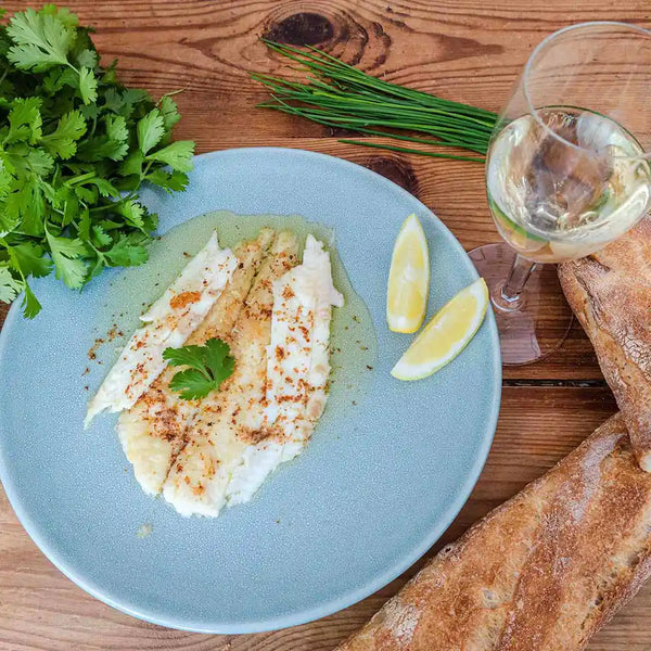The prepared sole meunière dish is served on a ceramic plate with a glass of white wine and some bread.