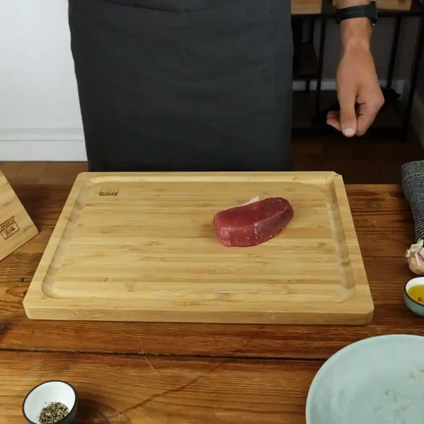 A frozen piece of beef tenderloin is resting on an antibacterial bamboo cutting board.