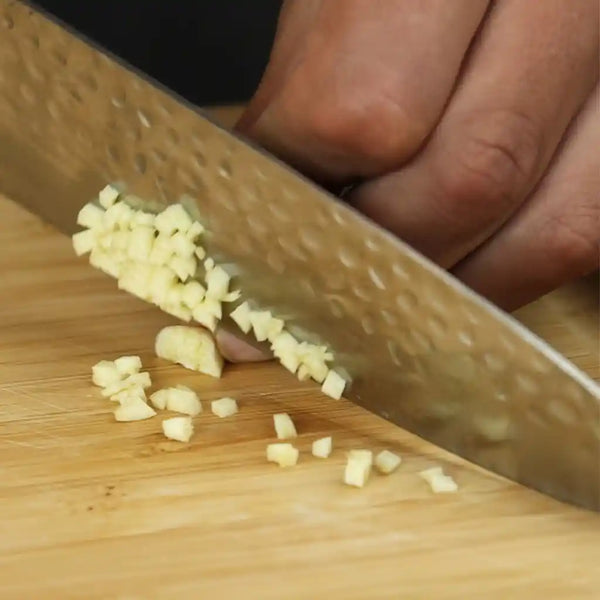 Chopping garlic in tiny dices with ease on an antibacterial bamboo cutting board with a hammered Japanese chef knife Gyuto.