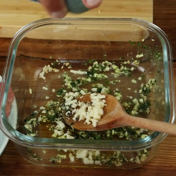Mixture of parmesan cheese, olive oil, chopped herbs and lemon juice in a glass bowl.