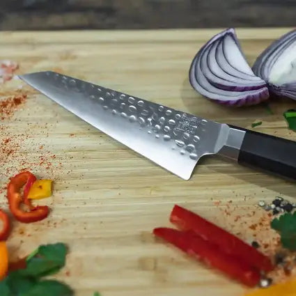 Le couteau universel Petty Bunka de KOTAI est présenté sur une planche à découper en bambou, entouré d'épices et de légumes finement coupés.
