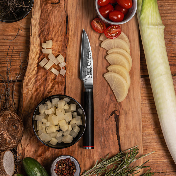 KOTAI's Paring Knife PAKKA Collection in Damascus steel, displayed on a wood cutting board with some ingredients next to it; tomatoes, lemon, herbs, ginger, etc.