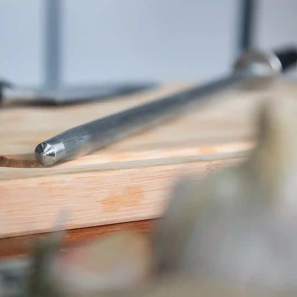 Camera is focusing on the pointed tip of the KOTAI's honing steel resting on the cutting board. 