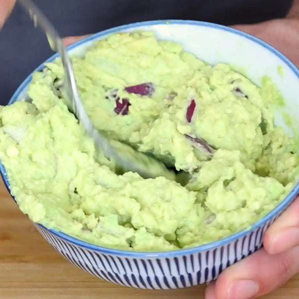 Model is mashing the avocado in a bowl with a fork.