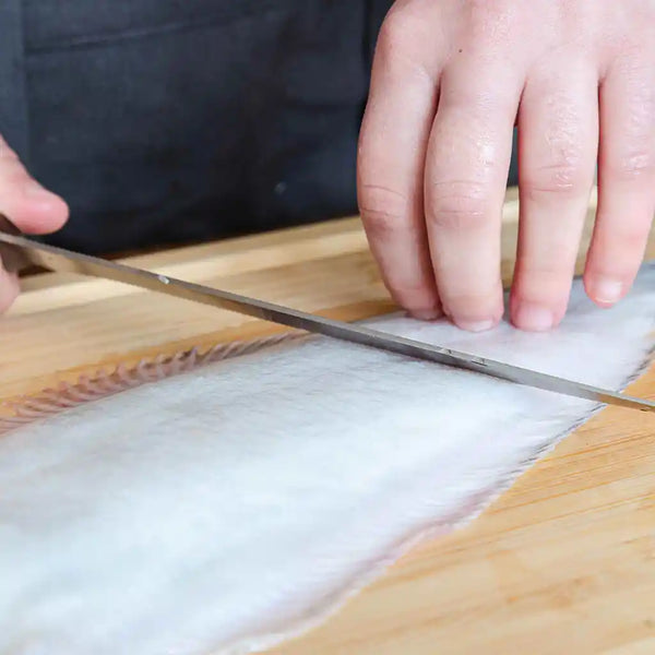 The model is scraping off the scales from the white part of the sole fish using KOTAI filet knife.