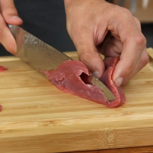The model is thinly slicing the piece of beef on a cutting board.