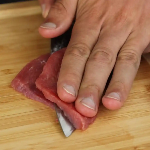 The model is thinly cutting the piece of beef on a cutting board. 