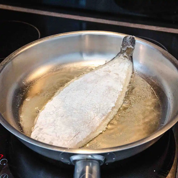 The fish is gently placed in a pan with heated oil. 
