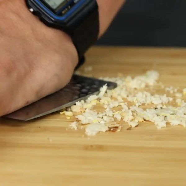 The model is using the flat blade profile of the cleaver knife to crush the pine nuts on the cutting board. 