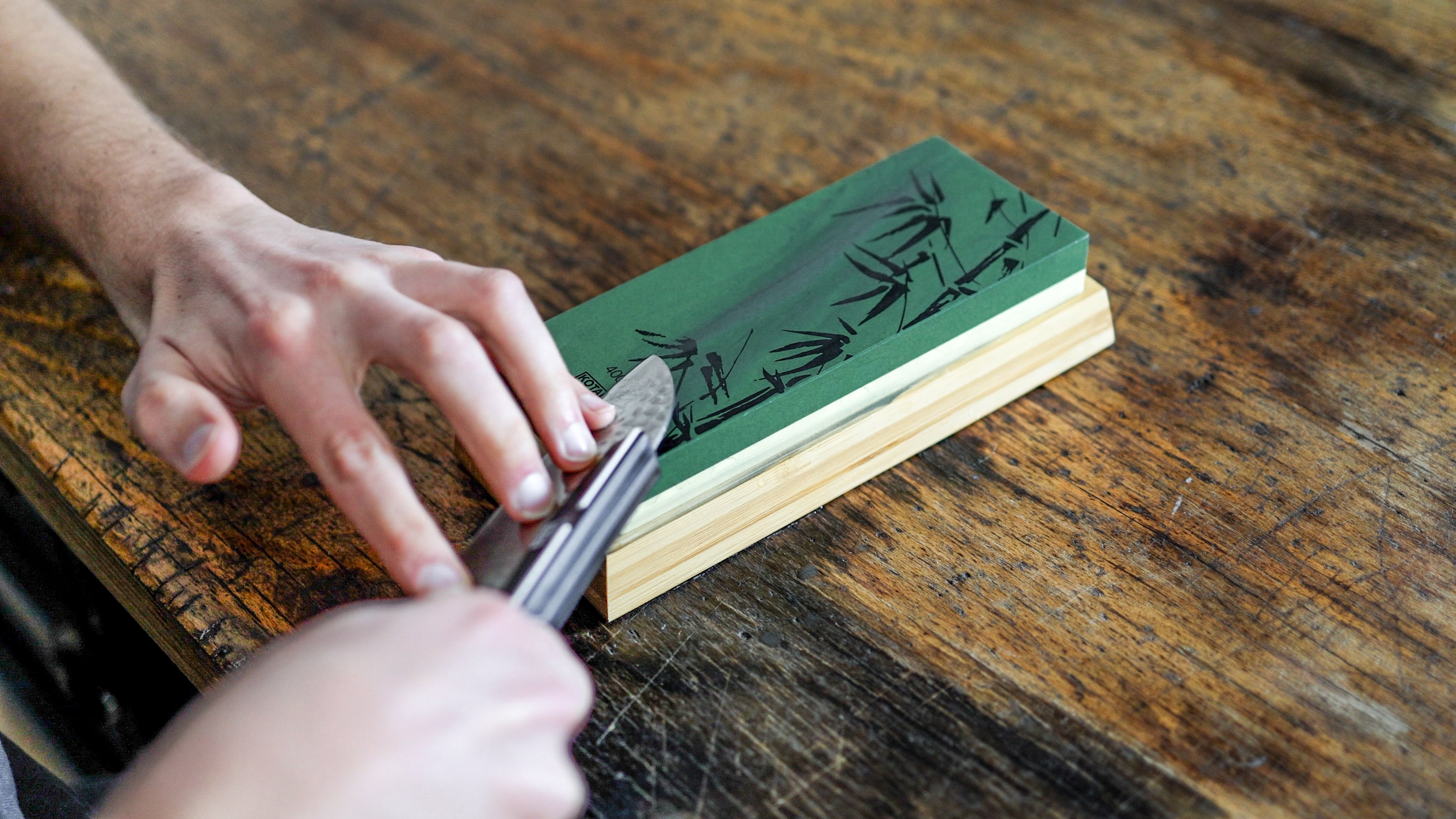 The model's hands are holding a KOTAI knife and preparing to sharpen it with a 400/1000 whetstone.