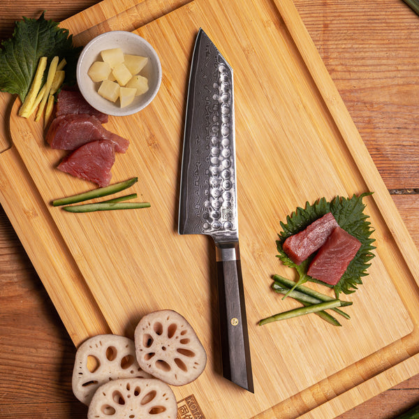 KOTAI's Santoku BUNKA Collection in Damascus steel, displayed on the KOTAI's bamboo cutting board with some ingredients displayed on it; herbs, fish, etc. 