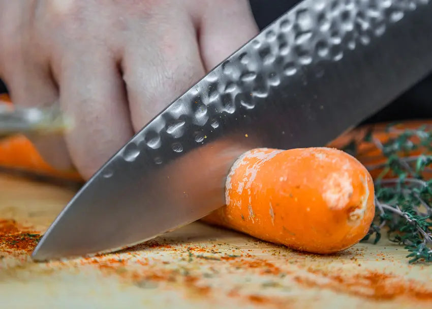 Couteau de chef Gyuto fait main coupant avec aise une carotte avec sa lame martelée.