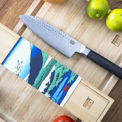 Le couteau Santoku avec sa belle lame martelée à côté de sa boite en bambou élégante.