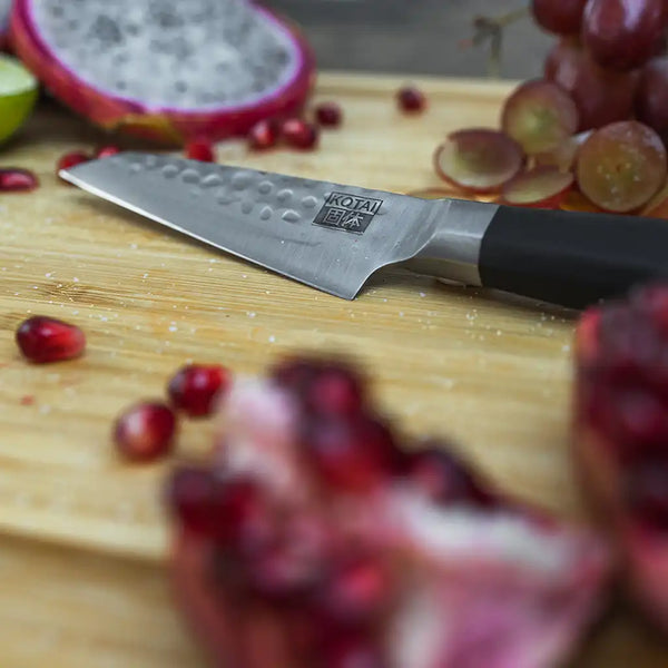 KOTAI's Paring knife BUNKA Collection displayed on the KOTAI's bamboo cutting board with some fruit such as a pomegranate or some sliced grapes.
