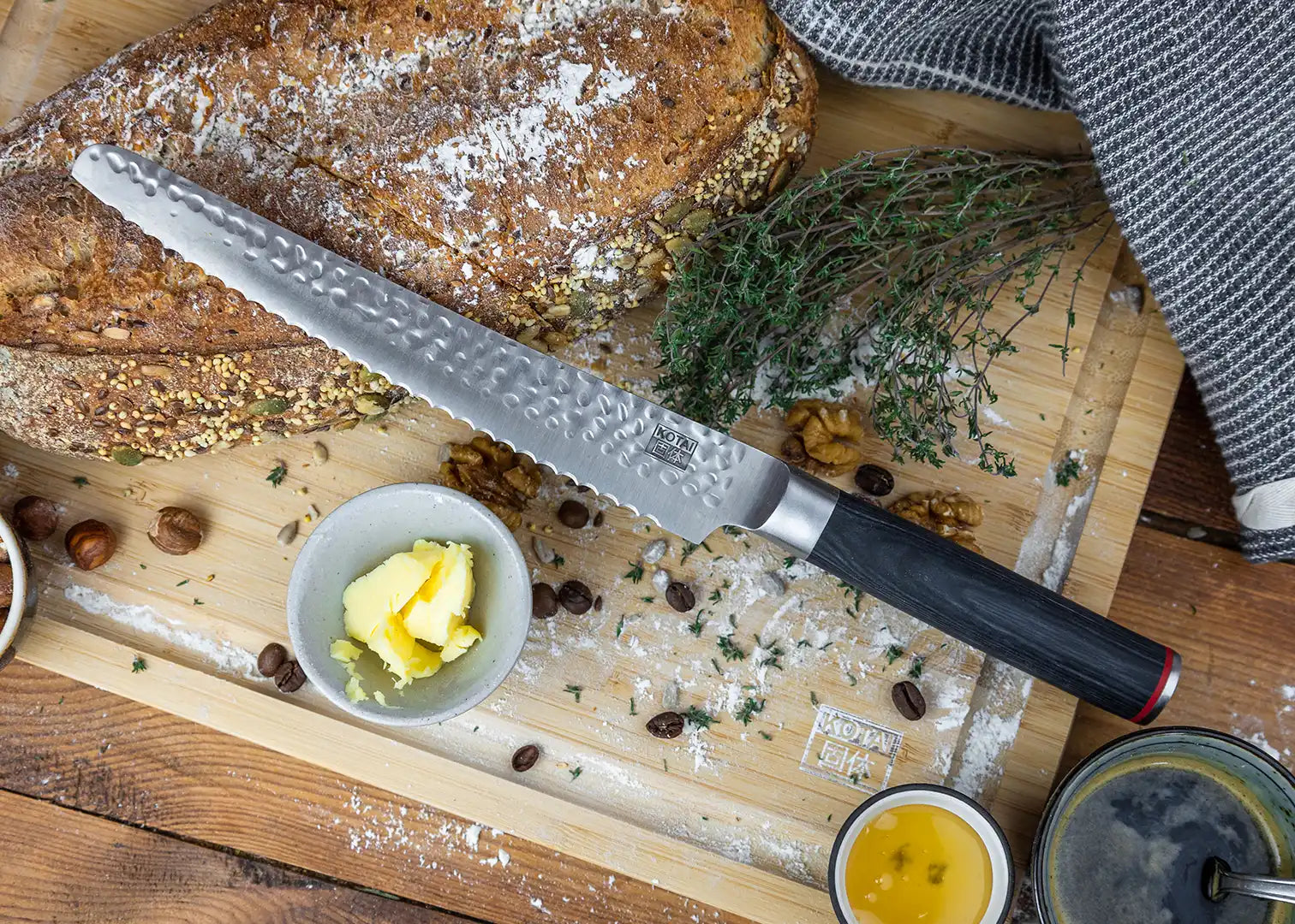 KOTAI's Bread Knife displayed on the KOTAI's cutting board with a grain bread and some condiments next to it, such as; butter, coffee, hazelnuts, etc.