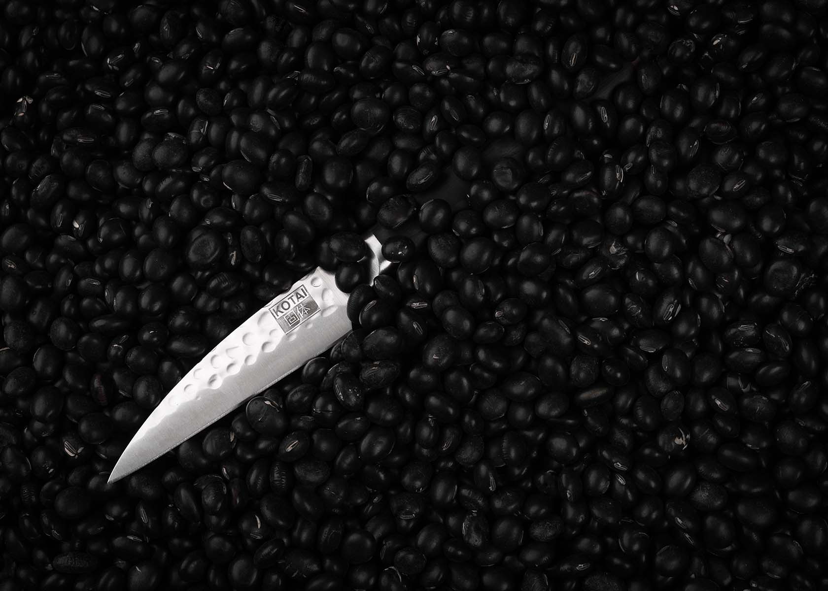 KOTAI Paring knife 90 mm blade and pakkawood handle hidden behind black beads background.